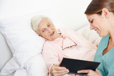 adult woman reading book to senior woman in bed